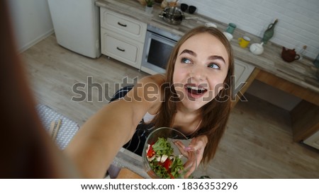 Vegan girl making photos, taking selfies with salad plate for social media on smartphone at kitchen. POV shot of blogger, taking pictures on phone, take selfie to her social accounts or video stories