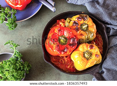 Baked sweet bell peppers stuffed with chicken or turkey, corn and herbs in cast iron pan, green stone background. Selective focus.