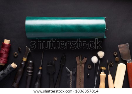 roll of green leather and various tools for handcrafting leather products. black leather background. Top view
