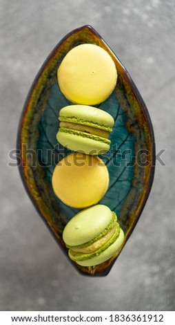 Vertical image. Yellow and green macaroons scattered on beautiful green leaf plate. Pistachio and passion fruit cakes