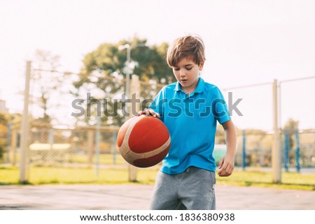 Focused cute boy athlete leads the ball in a game of basketball. A boy plays basketball after school. Sports, healthy lifestyle, leisure