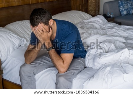 Stressed, depressed or grieving man sitting on bed covering face with hands and crying at home. Worried and frustrated male suffering depression or life crisis feeling desperate and helpless Royalty-Free Stock Photo #1836384166