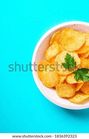 Fried corrugated golden potato chips with parsley leaf in wooden bowl on turquoise background, top view