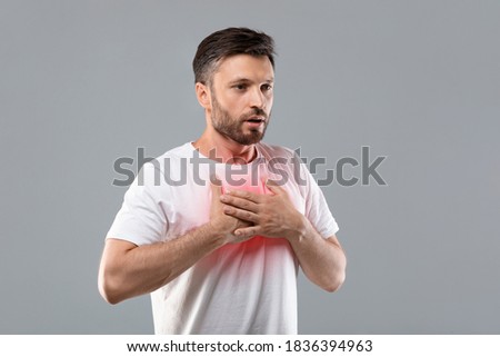 Breathing problem. Sick middle-aged man with chest pain touching inflammated zone and looking at copy space, grey studio background. Bearded man suffering from pneumonia. COVID-19 concept Royalty-Free Stock Photo #1836394963