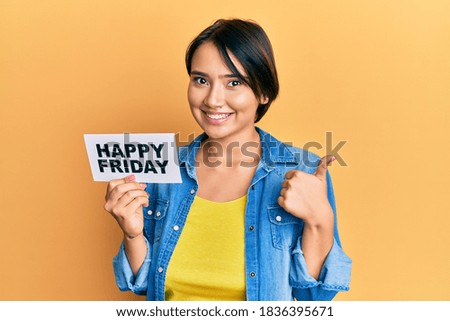 Beautiful young woman with short hair holding happy friday message paper smiling happy and positive, thumb up doing excellent and approval sign 