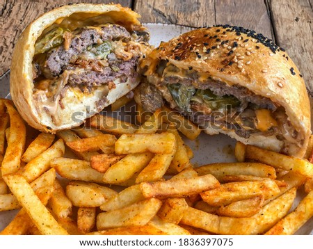 halved hamburger and french fries on plate on the wooden table