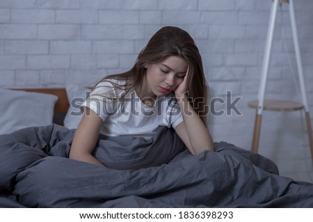 Winter depression concept. Sad young woman with seasonal affective disorder or depression sitting alone in her bed. Unhappy lady overwhelmed with negative thoughts, suffering from mental illness Royalty-Free Stock Photo #1836398293
