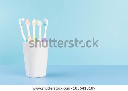Toothbrushes in a glass on​ light​ blue background.​ Dental health care and oral hygiene concept. Copy space.