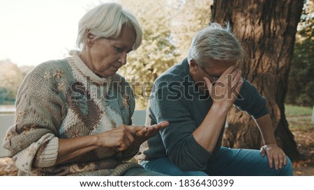 Elderly worried couple sitting on the bench in despair. Woman counting last coins. High quality photo