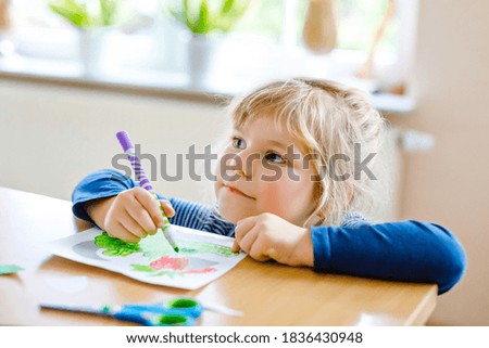 Little toddler girl painting animals and using scissors. Concept of activity of children during pandemic corona virus quarantine. Child learning colors with parents at home