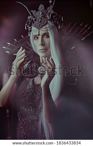 A portrait of a stately and beautiful old woman with long gray hair, in a rich headdress and a rich black dress against a dark background. Black Queen, Witch. Halloween.