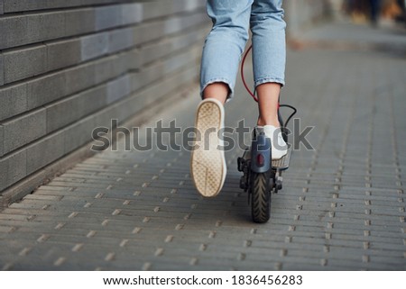 Close up view of girl in casual clothes that riding electric schooter outdoors at sunny daytime.