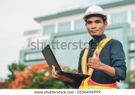 construction engineer has a laptop in hand and a thumbs up with the building site background