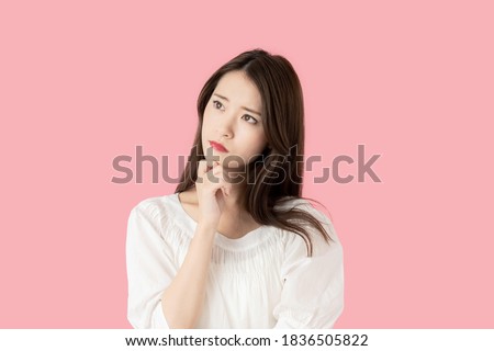 Thinking young asian woman in front of pink background.