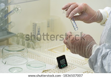 Scientist in protective white coat, mask and gloves analyzes a virus or bacteria sample in a laboratory with vials, glass flasks and chemicals. Medical lab test, new vaccine research or development Royalty-Free Stock Photo #1836507007