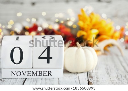 White wood calendar blocks with the date November 4th and autumn decorations over a wooden table. Selective focus with blurred background. 