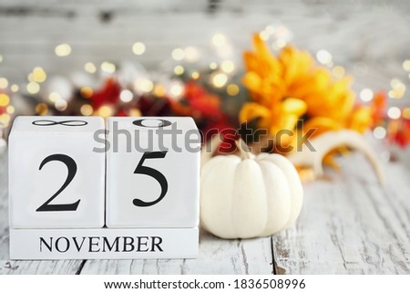 White wood calendar blocks with the date November 25th and autumn decorations over a wooden table. Selective focus with blurred background. 