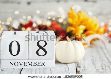 White wood calendar blocks with the date November 8th and autumn decorations over a wooden table. Selective focus with blurred background. 