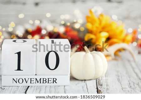 White wood calendar blocks with the date November 10th and autumn decorations over a wooden table. Selective focus with blurred background. 