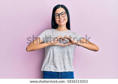 Beautiful young woman wearing casual clothes and glasses smiling in love doing heart symbol shape with hands. romantic concept. 