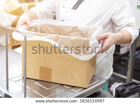 A worker in production weighs products in a box on scales, packing and sorting products by weight, industry