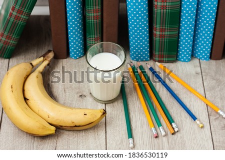 pile of books in colorful covers, bananas, pencils and glass of milk on wooden table. Back to school distance home education.Quarantine concept of stay home