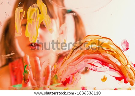Cute young girl painting artwork on glass. Happy childhood, painting lessons concept. Selective focus on finger. Horizontal image.