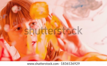 Close up beautiful young girl painting artwork on glass with colorful hands and finger. Happy childhood, art, painting lessons concept. 