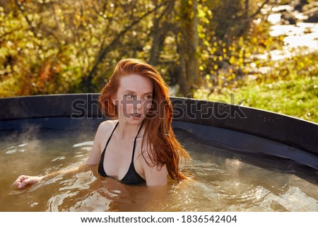 young charming redhead woman is relaxing in hot tub whirlpool jacuzzi outdoor in the nature, sit inside of bath, resort spa retreat