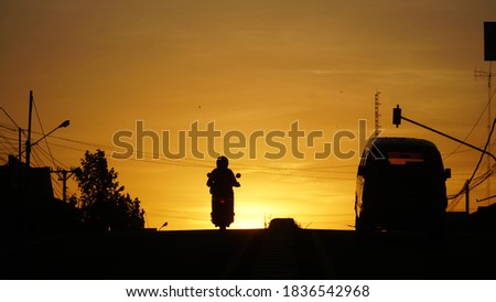 Silhouette of motorbikes and cars on the highway against the background of the orange twilight sky