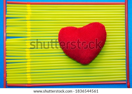 red plush heart on yellow drinking straws, in a frame of reds, on blue background