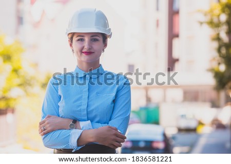 The stylish woman architect in hardhat is standing in the city
