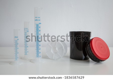 Dark room equipment for film photography:  graduated cylinder, syringe, funnel, self winding reel for 35mm and 120 format film, developing tank and other parts on white background.