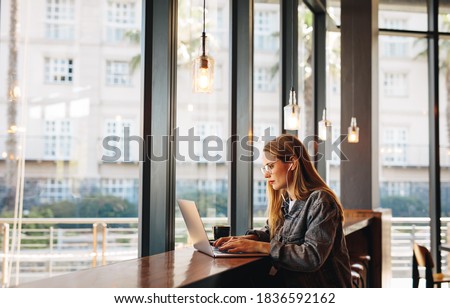 Woman sitting at a cafe table working on laptop. Woman doing her work sitting at a coffee shop. Royalty-Free Stock Photo #1836592162