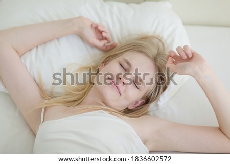 Pretty woman waking up in the morning and stretching in bed after a good night's sleep.