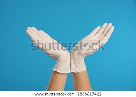 Doctor wearing medical gloves on light blue background, closeup