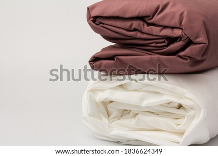 Stack of folded clean white and maroon bed sheets and pillowcases on white; background; closeup.