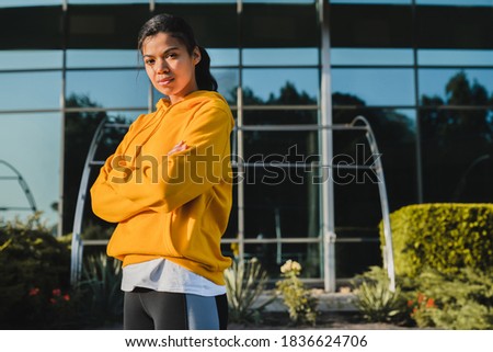 Young beautiful mixed race girl standing against glass building in sporty outfit