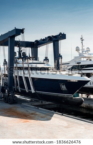 Super Yacht hauled out in shipyard, being lifted by industrial crane for refit or maintenance yard period  Royalty-Free Stock Photo #1836626476
