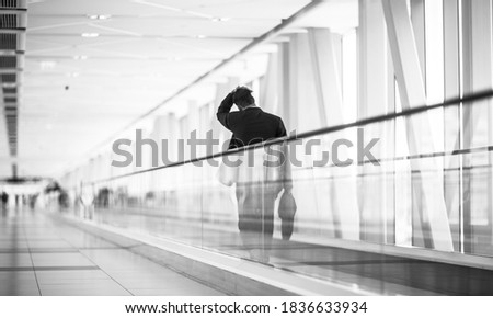 Weary businessman pedestrian walking alone on moving walkway inside a modern terminal link. Black and white. Royalty-Free Stock Photo #1836633934