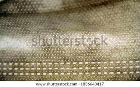 Macro image of a three layered surgical mask illuminated from behind, with detail of stitches