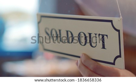 Close up of human hand hanging sold out sign on glass door of cafe or store. Owner putting sold out sign on window in local market or bakery store. Small business concept