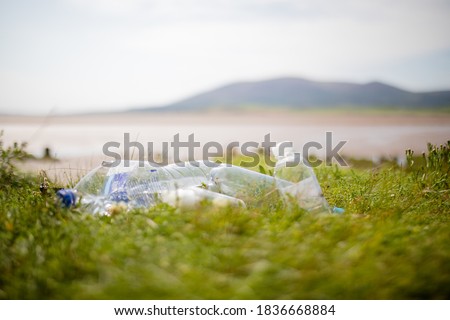Picture of a couple of empty plastic bottles abandoned on the grass with a blurry open land and a mountain in the background