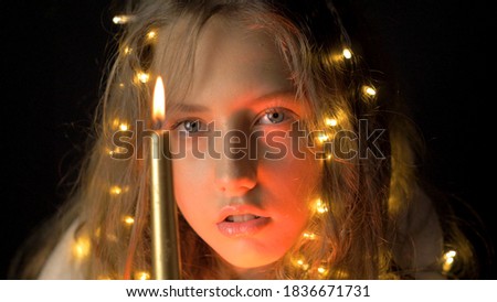 Close up portrait of a blonde girl in funny pajamas. Christmas lights and candles. Make a wish. Christmas lights. New year and Christmas eve. Winter holidays. Sparkling garland