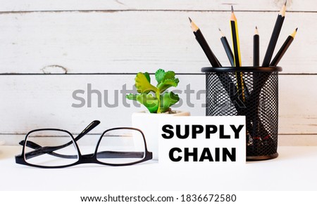 SUPPLY CHAIN written on a white business card next to pencils in a stand and glasses. Nearby is a potted plant. Internet education