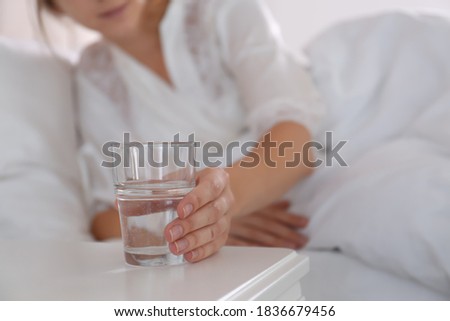 Woman taking glass of water from nightstand in bedroom, closeup