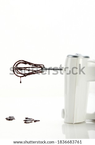Handheld white small egg beater blender with chocolate dripping off after being used for a desert. White background and studio lighting. Royalty-Free Stock Photo #1836683761