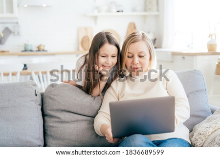 Smiling mom and daughter surf in a laptop on the couch at home. Having fun online, internet education, working from home