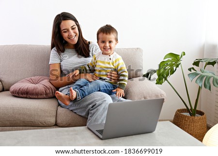 Stay at home mom working remotely on laptop while taking care of her baby. Young mother on maternity leave trying to freelance by the desk with toddler child. Close up, copy space, background