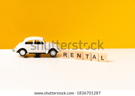 Toy white car on a white table with a yellow background, the inscription of wooden blocks. The concept of a rental car and car sharing.